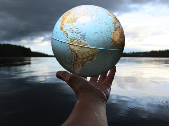 Entre ombre et lumière, un globe tenu à la main rappelle une évidence : la mondialisation ne disparaît pas, mais se redéfinit, entre tensions géopolitiques et interdépendances inévitables