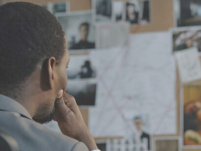 A dedicated police officer, immersed in the task of unraveling a cybercrime case, contemplates the investigative board with a pensive expression