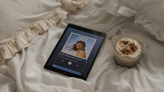 A tablet sitting on a bed next to a cup of coffee, Playing Taylor Swift