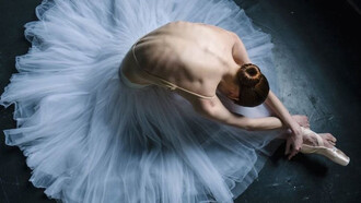 A ballet dancer gracefully leans towards the floor, her focus on her feet and form