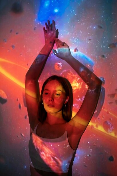 A young woman standing within a projection of the universe, surrounded by surreal landscapes, cosmic energy, and dreamlike spaces