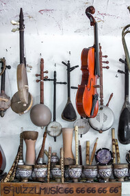 A variety of colorful guitars and other musical instruments, including violins, displayed on the wall
