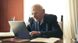 A senior man in a gray blazer is working on his laptop while enjoying coffee, illustrating demographic change and the growing digital engagement of older generations