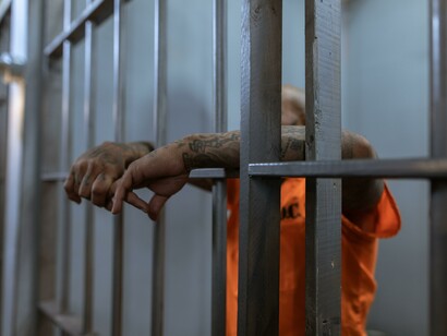 A person in orange with their hands resting on metal bars
