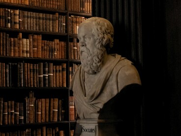 A bust of Socrates standing among rows of books, representing the historical relationship between knowledge, literature, and intellectual thought
