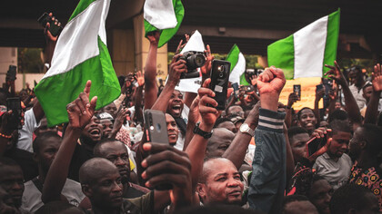 In the heart of Nigeria, amidst waving flags, individuals gather with their phones, showcasing how mobile technology has revolutionized communication, connecting loved ones effortlessly and bridging geographical barriers