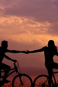 A woman on a bike reaching out to take the hand of a man riding behind her, both enjoying a moment of connection