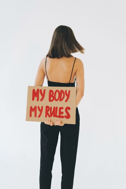 Vista traseira de uma mulher segurando um cartaz sobre 'Meu corpo, minhas regras'
