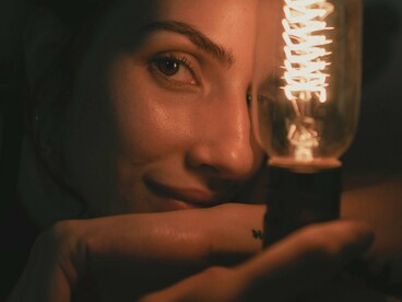 Uma mulher encara a luz no meio da escuridão, enquanto sombras atravessam o enquadramento. Como na letra de “Joshua”, a claridade aqui deixa de esconder aquilo que precisa ser enfrentado