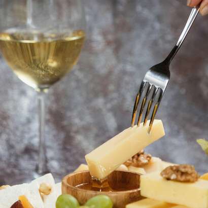 Cheese dipped in honey on a rustic platter with snacks and white wine, overhead view