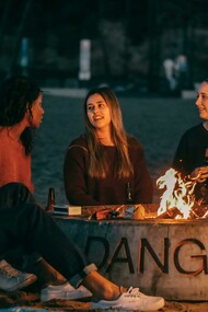 A group of friends sits around a fire pit, sharing stories in a circle during a community storytelling event