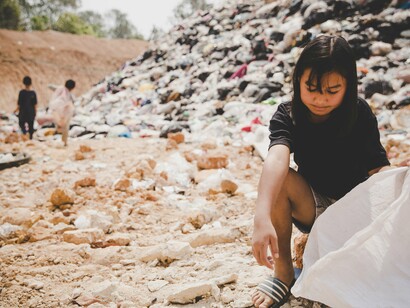 Amid a barren landscape of dust and discarded waste, three children labor in silence, wearing tattered clothes and tired expression—a reality in which education and play are luxuries, and work is a necessity