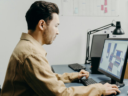 A man in a brown long-sleeve shirt working on a 3D design in a professional business environment