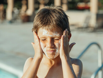 Un niño se frota la cara con protector solar, ya que es esencial para salir al sol