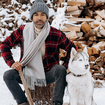 A man and his loyal dog resting near stacked firewood on a snowy day
