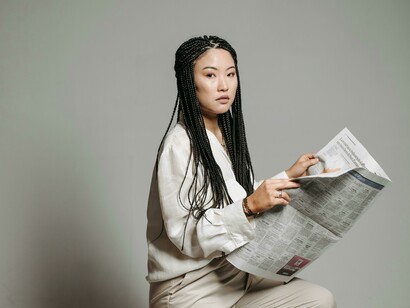 A woman with braided hair focused on reading a newspaper