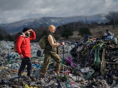 Man and woman hikers with walking poles on landfill, environmental and pollution concept 