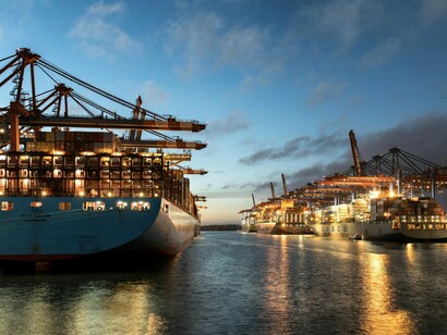 Massive cargo ships heading towards the dock beneath a darkening sky, representing the fragile lifelines of global trade