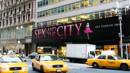 Manhattan em cenário típico de Sex and the City e cartaz em referência à personagem principal.  O seriado contando a história de quatro mulheres solteiras em Nova York atraiu uma legião de fãs, ganhou prêmios e se tornou um marco ao ser um seriado voltado para as mulheres, que falava de sexo e não tinha medo de discutir assuntos considerados tabus na época