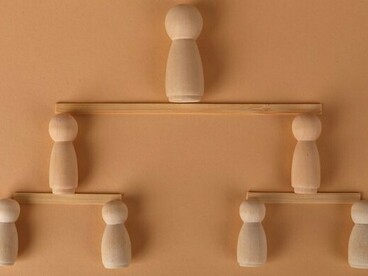 Wooden figures arranged in tiers beneath a single figure at the top, representing the hierarchy and authority that shape the world of work