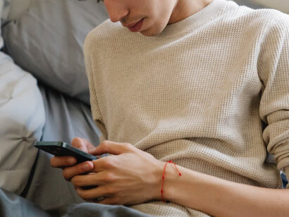 Ragazzo sul proprio letto con gli occhi fissi sul cellulare 