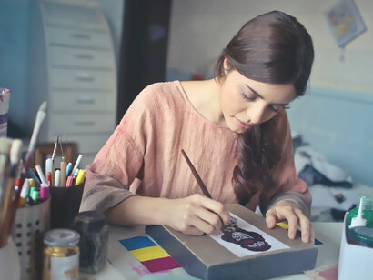 Engrossed in her artistic pursuit, a woman paints at a table surrounded by an array of paintbrushes