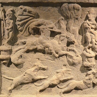 Una raffigurazione di Mitra con una tunica corta e un mantello svolazzante, in sella a un cavallo. Il dio, la cui testa è danneggiata, scaglia una freccia dal suo arco.  Museo Schloss Fechenbach, Dieburg, Germania 