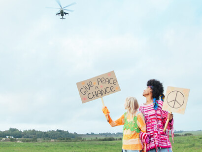 A military helicopter flies over the signs a couple are holding up for peace