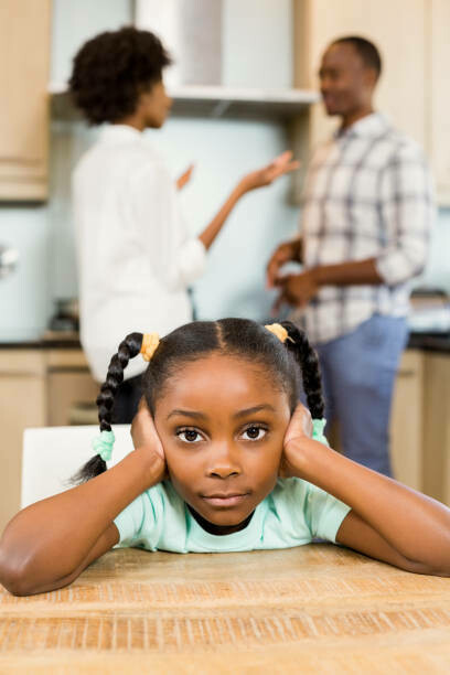 A child sits at the dinner table, covering his ears as his parents argue