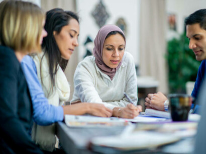 In a dynamic startup environment, a group of young entrepreneurs from various backgrounds, including a migrant with a turban, work together on innovative projects