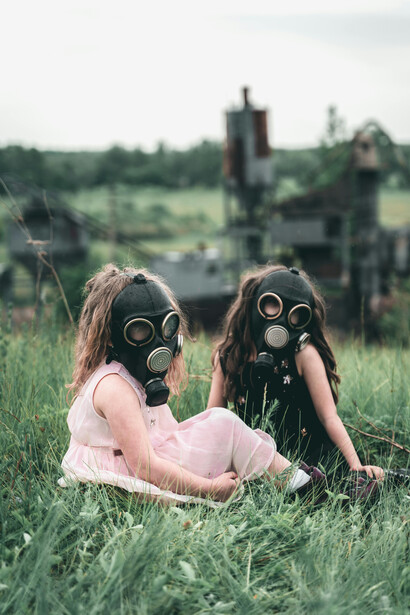 Wearing gas masks, children sit closely together on a patch of grass, their eyes fixed on the radioactive forest beyond