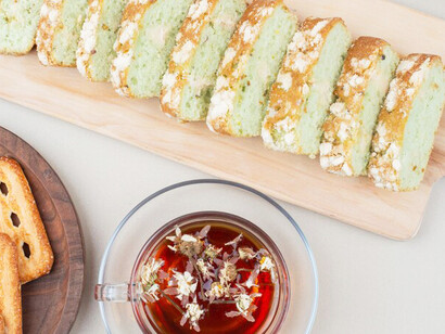 A charming arrangement of warm zucchini cake slices, biscuits, and a cup of tea, inviting you to savor a moment of bliss on a pristine white surface