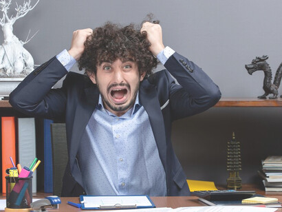 A stressed and overwhelmed businessman is shown sitting at his desk, clutching his head in agitation, illustrating the impact of burnout in the professional environment