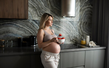 A medium shot of a pregnant woman enjoying a fruit bowl, emphasizing the benefits of nutritious food choices during pregnancy for both mother and baby