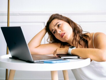 An exhausted professional resting her head beside an open laptop, representing the burden of financial stress on workplace focus and productivity