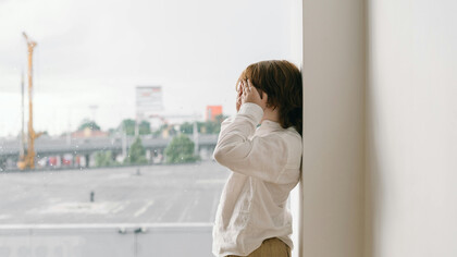 A child next to a window covers his eyes with his hands