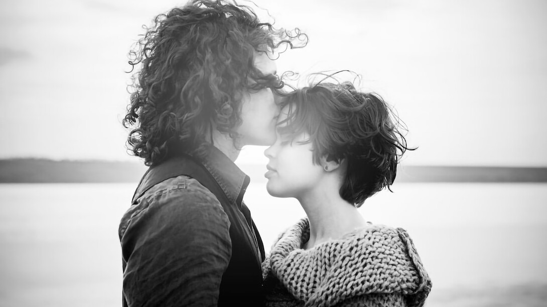 Grayscale of man kissing woman's forehead