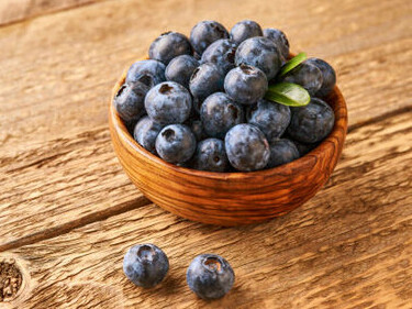 A rustic wooden table showcases a charming basket filled with vibrant, succulent blueberries