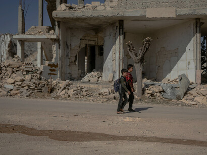 In Idlib, Syria, two students walk down an unpaved road surrounded by the ruins of buildings destroyed by years of war