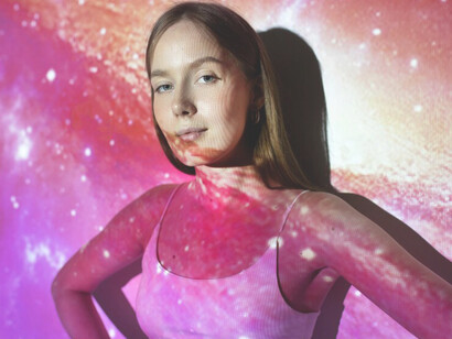 A young woman stands amidst a universe texture projection, symbolizing the essence of feminine energy and its transformative significance