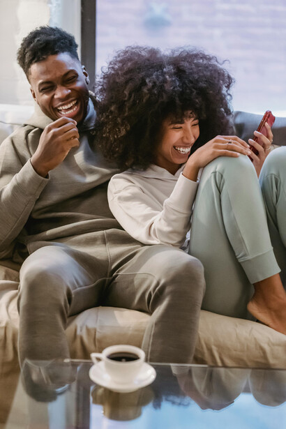 A happy Black couple sits together on a couch, enjoying a vertical microdrama on their smartphone