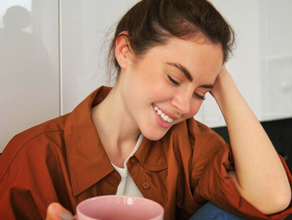 The warmth of a cozy moment as a joyful young woman savors her coffee in the kitchen, wearing a tender smile while lost in peaceful daydreams