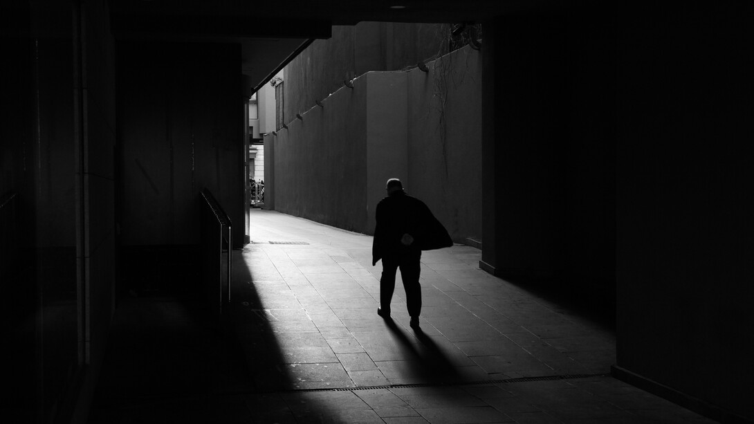 Una figura solitaria avanza por un pasaje oscuro hacia una zona iluminada, dejando una larga sombra sobre el suelo