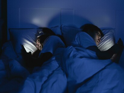 A woman lies on her bed while using her mobile phone