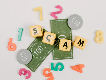 Letter tiles spelling “scam” prominently across a tabletop, symbolizing the fraudulent tactics that can hide behind trusted support channels