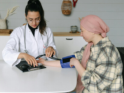 A female doctor checks a female cancer patient' blood pressure, both are sitting at a table