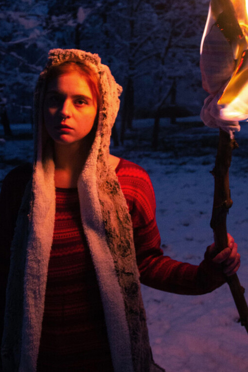 Mulher se aquece com tocha de fogo em um bosque nevado. O fogo talvez seja a nossa primeira dádiva
