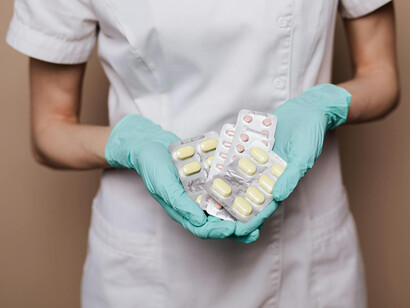 Mujer con uniforme médico y guantes quirúrgicos muestra blísteres de medicamentos