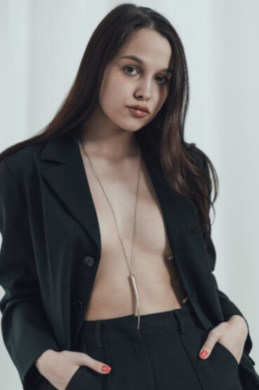 A woman confidently poses in a black suit, wearing nothing underneath