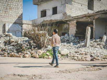 A lone boy makes his way through the rubble-strewn streets of Syria, surrounded by the ruins of homes destroyed by explosions